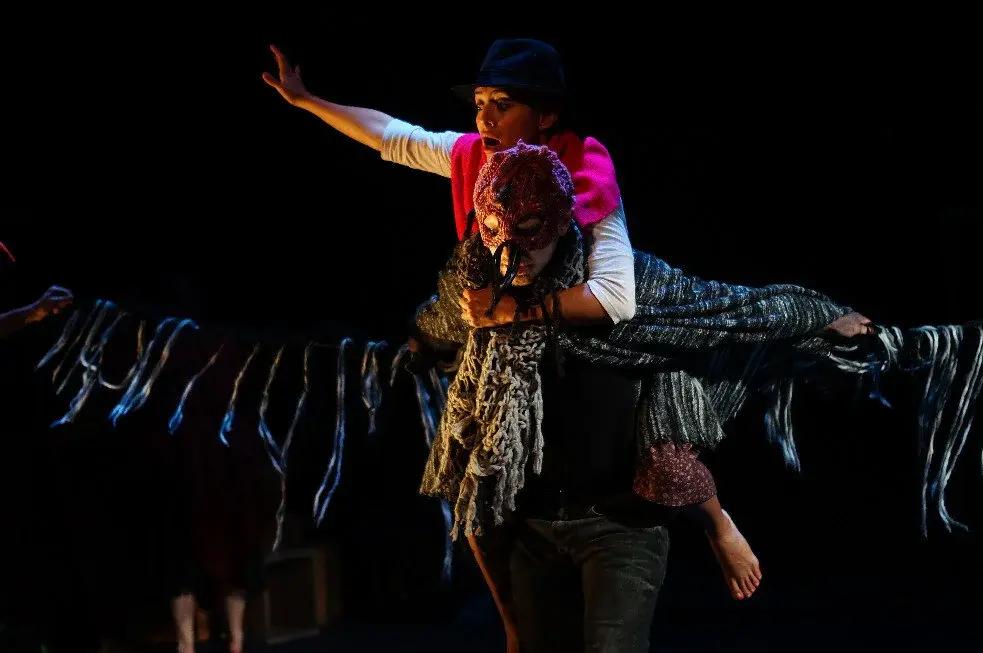 A DAT performer in flight with outstretched woven wings on a darkened stage